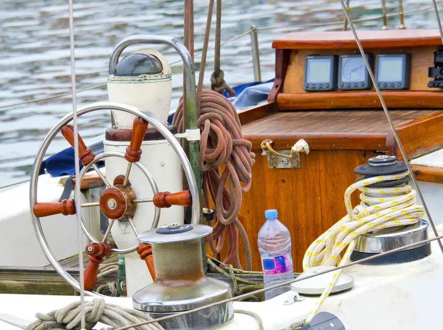 Close-up of a sailboat deck with wooden steering wheel, ropes, and navigation instruments.
