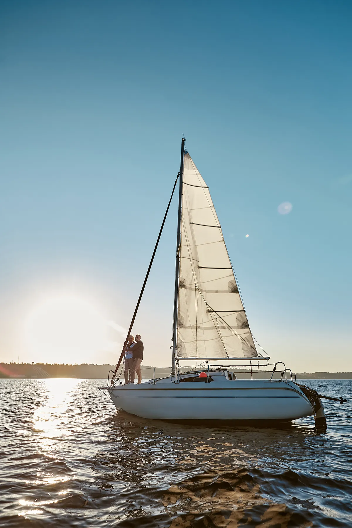 Romantic senior couple enjoying amazing sunset while standing on the side of sail boat