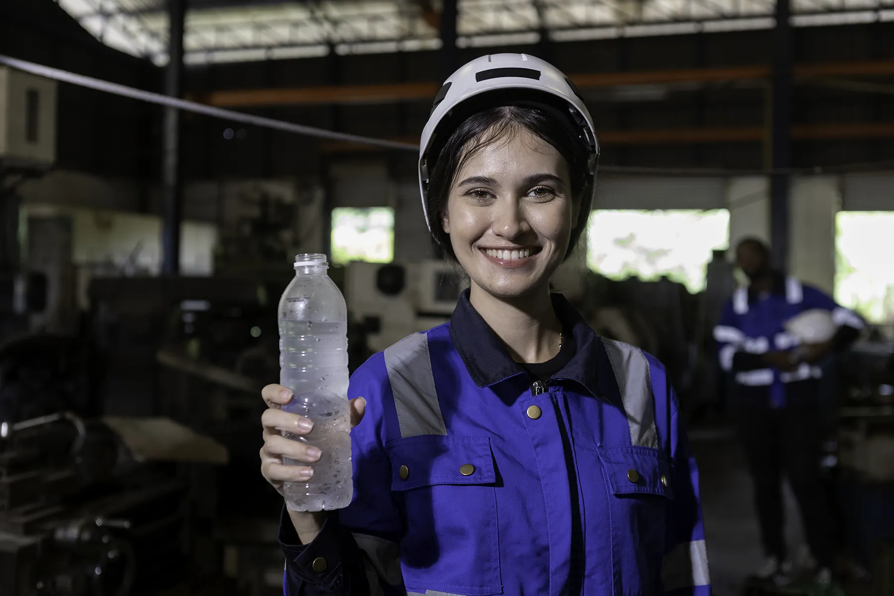 Female engineer smiling and holding a bottle of clean water in an industrial setting, representing access to pure, desalinated water with ECHOTec Watermakers.
