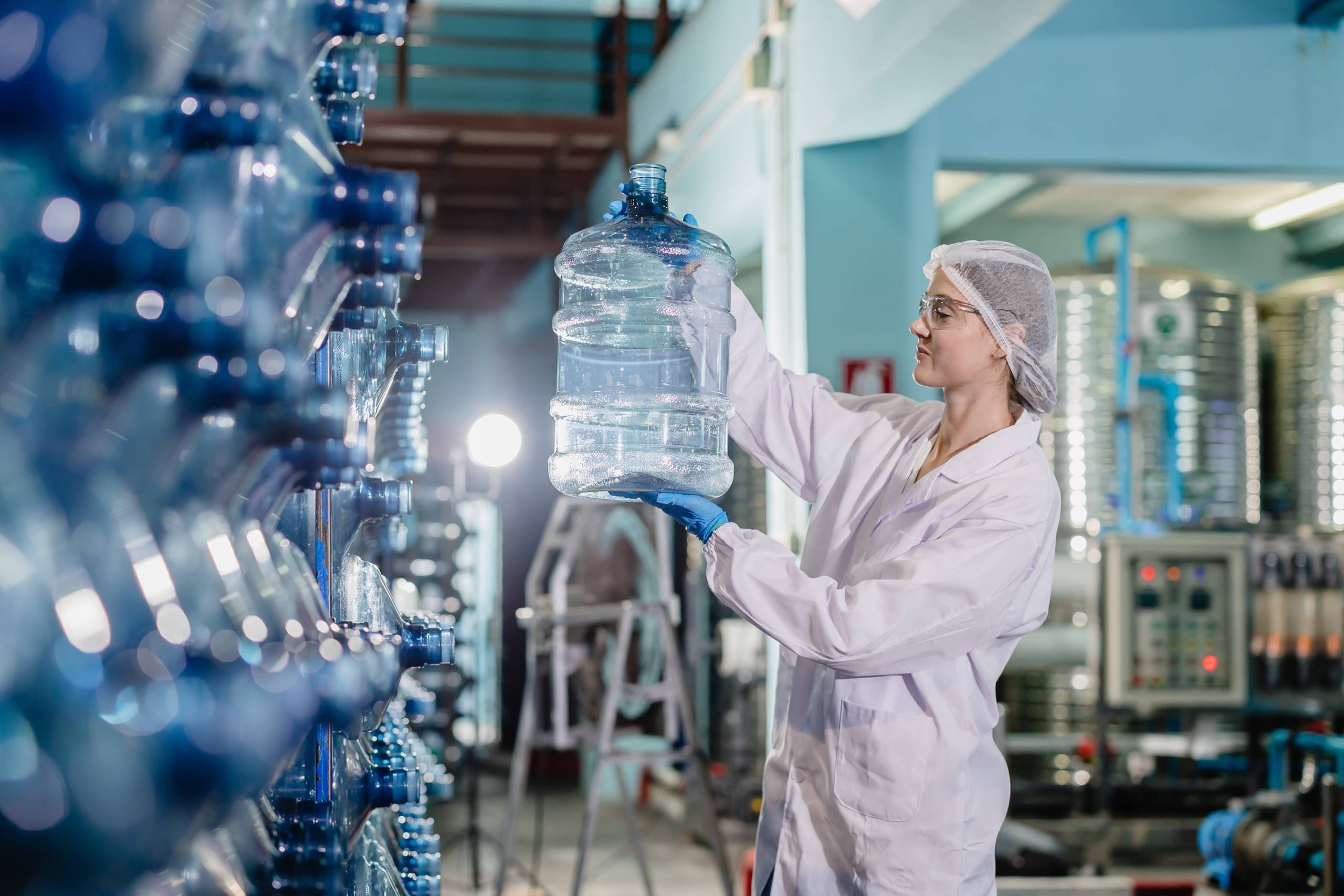 Women worker in drinking water factory working check cleanliness of water bottle gallon storage warehouse.