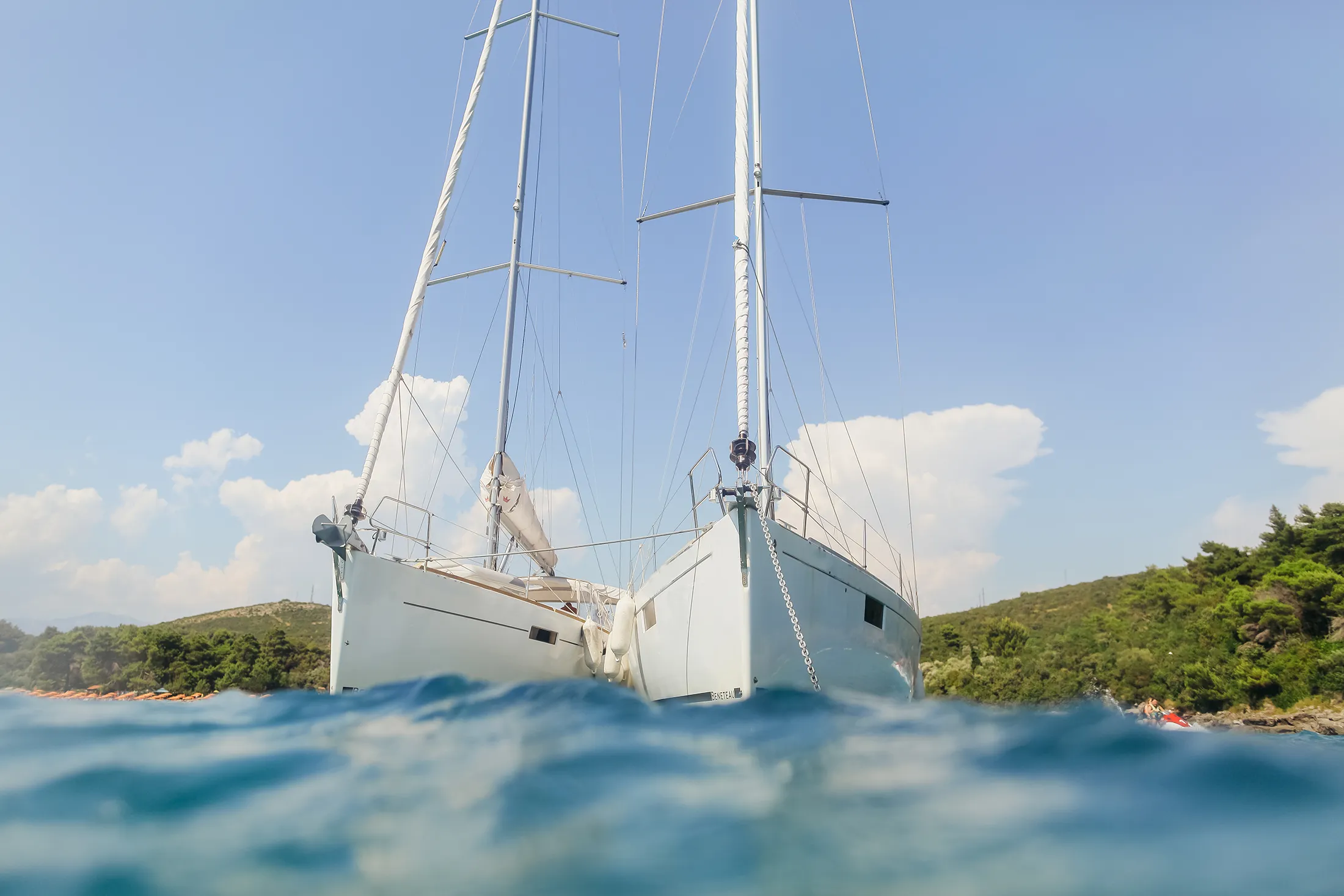 Two sailboats anchored near the shoreline, floating on clear blue water under a bright sky.