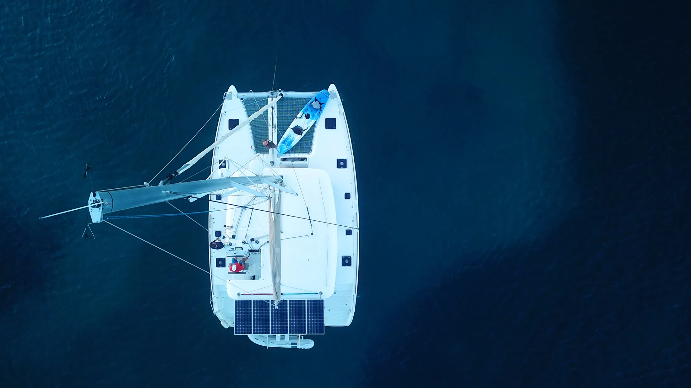 Aerial view of a sailing catamaran with solar panels cruising on open water, showcasing off-grid marine power and sustainable sailing.
