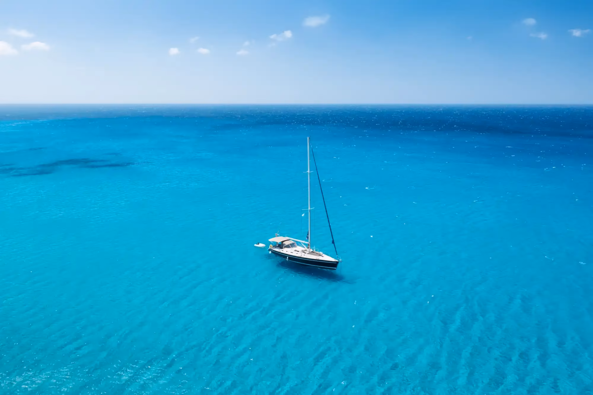 aerial-view-sailboat-anchored-in-turquoise-ocean-echotec-watermakers. Aerial view of a sailboat anchored in clear turquoise open ocean water under a bright blue sky